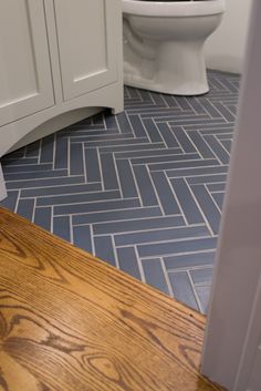 a white toilet sitting next to a wooden counter top in a bathroom with blue tiles on the floor