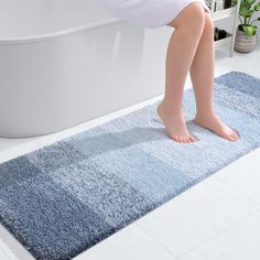 a child standing on a blue rug in front of a bathtub