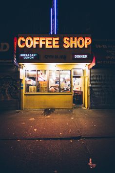 a coffee shop lit up at night on the side of the street with no one in it