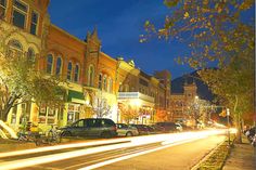 a city street at night with cars driving down the road and buildings in the background