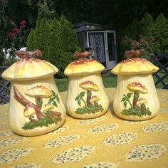 three ceramic mushrooms sitting on top of a table covered in yellow cloths and trees