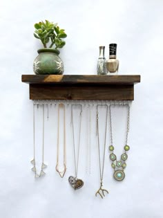 a wooden shelf with necklaces hanging from it's sides and a potted plant on top