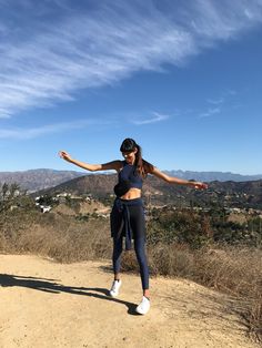 a woman standing on top of a dirt hill with her arms spread out in the air