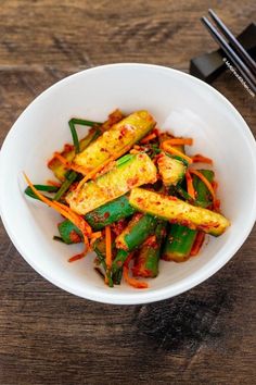 a white bowl filled with vegetables and chopsticks on top of a wooden table