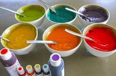 six cups with different colors of paint in them and two spoons on the side