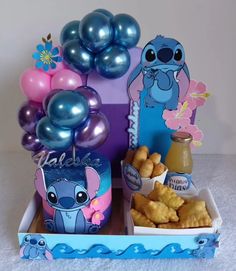 a box filled with lots of food on top of a white table covered in balloons