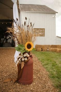 a sunflower in a brown vase sitting on the side of a building with hay