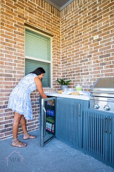 a woman opens the door to an outdoor kitchen with blue cabinetry and brick walls