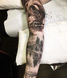 a man's arm with a bear and mountain scene tattoo on the left forearm