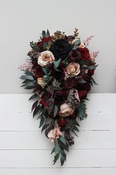 a bridal bouquet with red, pink and black flowers on a white wooden surface