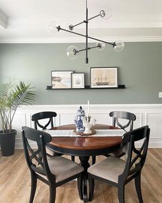 a dining room table with four chairs and a vase on top of it, in front of a green wall