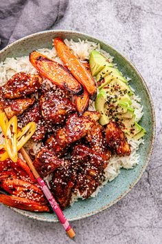 a bowl filled with meat, rice and veggies next to chopsticks