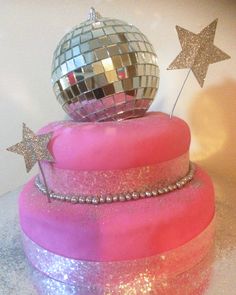 there is a pink cake that has a disco ball on top and stars around it