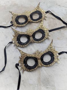 Wide-eyed and wise, owls perceive what other creatures do not, the perfect spirit to carry with you to a masquerade. This lace mask is stiffened and painted by hand in gold on the feathers and beak for extra intrigue. One size fits most. Ties with satin ribbon. Black Masks For Halloween Gift, Black Halloween Masks As Gifts, Black Masquerade Mask For Halloween Gift, Gothic Gold Masquerade Mask For Carnival, Gold Gothic Masquerade Mask For Carnival, Black Fantasy Costume Accessories As Gift, Gothic Gold Costume Accessories For Masquerade, Black Fantasy Eye Mask, Fantasy Style Black Eye Mask