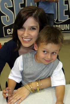 a woman sitting next to a little boy on top of a white table in front of a sign