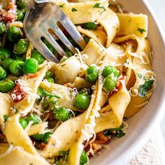 a white bowl filled with pasta, peas and parmesan cheese topped with a fork