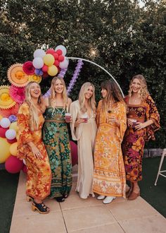 four women standing in front of a arch with balloons and streamers on the wall