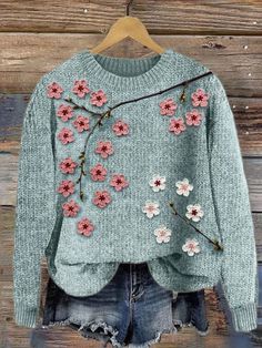 a sweater with flowers on it hanging from a hanger in front of a wooden wall