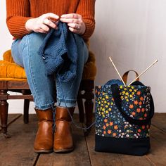 a woman sitting on a chair next to a purse and knitting needles in her hands