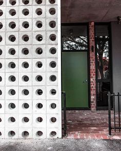 a green door is in front of a white wall with round holes on the side