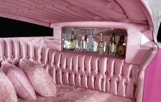 the inside of an old pink car with pillows and bottles on it's back