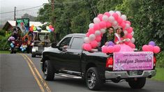 two women riding in the back of a pickup truck with balloons on it's bed