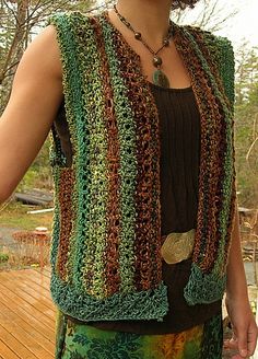 a woman standing on a deck wearing a green and brown crocheted vest