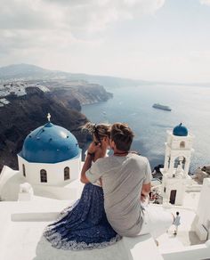 a man and woman sitting on the edge of a building looking out at the ocean