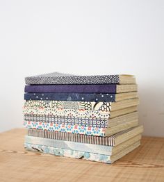 a stack of folded books sitting on top of a wooden table next to a white wall