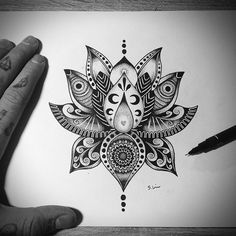 a drawing of a lotus flower on paper with a pen in the foreground and a person's hand next to it