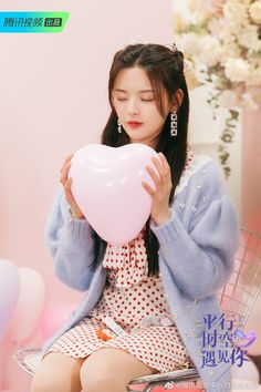 a woman holding a heart shaped balloon in front of her face while sitting on a chair