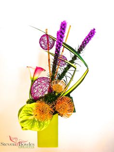 a green vase filled with purple and yellow flowers