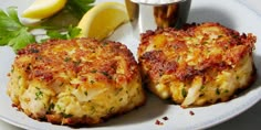 two crab cakes on a plate with lemon wedges