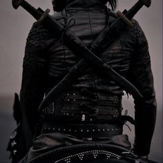 the back of a man with two large swords on his shoulder and wearing leather armor