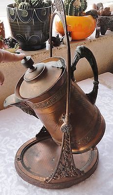 an old fashioned coffee pot on a stand next to some pumpkins and cacti