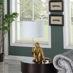 a gold monkey lamp sitting on top of a table next to a chair and window