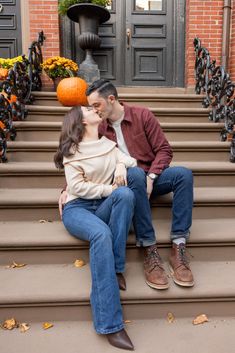 a man and woman sitting on the steps kissing with pumpkins in front of them