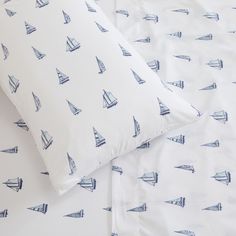 two pillows with blue sailboats on them sitting next to each other in front of a white sheet