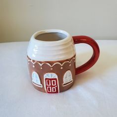 a coffee mug with a house painted on the outside and red rim around the inside