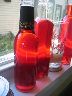 three bottles are sitting on a window sill, one is red and the other is pink