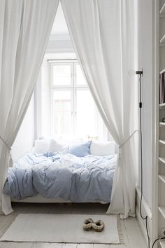 a bed sitting under a window next to a white book shelf filled with lots of books