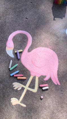 a pink flamingo drawn in chalk on the ground with crayons around it