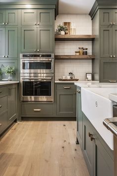 a large kitchen with green cabinets and white counter tops, wood flooring and open shelving