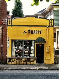 a yellow storefront with tables and chairs on the sidewalk in front of it that says le happy