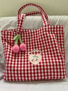 a red and white gingham bag sitting on top of a bed next to a stuffed animal