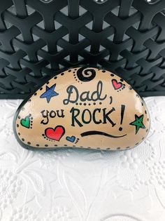 a rock with the words dad you rock written on it next to a black purse