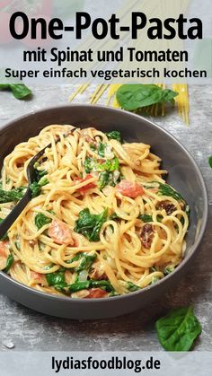 a bowl filled with pasta and spinach on top of a table next to tomatoes