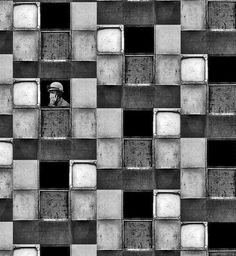 black and white photograph of a man looking out from a window in a tiled wall