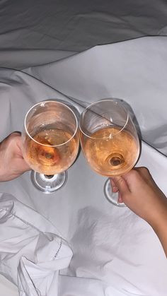 two people toasting with wine glasses on top of a white sheet covered bedspread