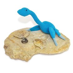 a blue toy lizard sitting on top of a rock next to some rocks and pebbles